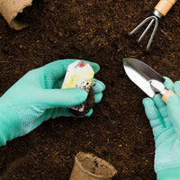 Hands in green gloves planting a Pink and Yellow Plantable Seed Paper Blank Gift Tags by Seed Bloom Gifts directly into rich brown soil.