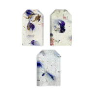 The image displays three individual stacks of Purple Blank Tags Plantable Seed Paper by Seed Bloom Gifts arranged in a white background, highlighting the varying placement of the embedded purple and blue dried petals and natural texture.