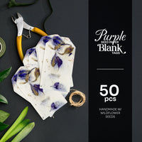 A dark, styled product photo displays a stack of Purple Blank Tags Plantable Seed Paper by Seed Bloom Gifts, a spool of twine, and pliers next to text indicating "Purple SEED PAPER BLANK TAGS 50 pcs".