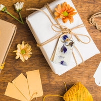 Purple Blank Tags Plantable Seed Paper by Seed Bloom Gifts tied to a white-wrapped gift with twine and accented by an orange mum flower.