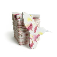 A colorful hummingbird sits atop a stack of memorial plantable seed paper, blending art with eco-consciousness
