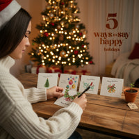 Woman writing a plantable holiday card by Seed Bloom Gifts with a decorated Christmas tree in the background