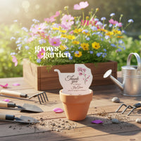 Terracotta pot with a thank you carriage shaped baby shower favor by Seed Bloom gifts, garden tools, and a planter of wildflowers on a wooden surface.