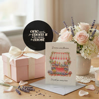 Mother's Day Bloom Card: Greeting card with flower shop illustration displayed next to a pink gift box with ribbon, fresh pink roses and lavender in a vase, with a quote bubble reading 'one card for mom's who mean the most