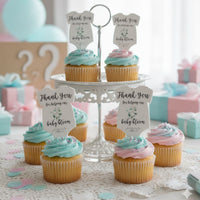 Cupcakes topped with pink and blue frosting are displayed on a tiered stand. Each cupcake features a gender neutral green onesie plantable seed paper baby shower favor by Seed Bloom gifts used as a topper, reading 'Thank you for helping our baby bloom.' The background includes wrapped gifts and pastel balloons.