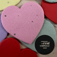 Heart-shaped fabric pieces in various colors with a black circular label indicating ' Embedded with real wildflower seeds'.
