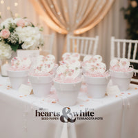 Decorative setup with white and pink flowers in terracotta pots on a table, branded 'hearts & white', Seed Bloom Gifts.