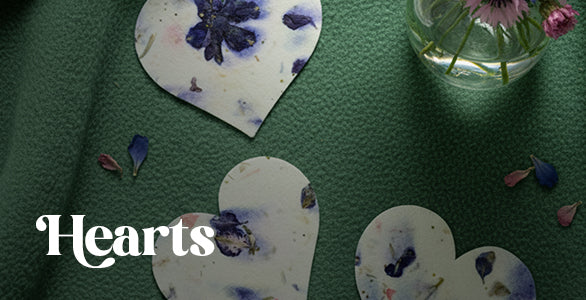 Heart-shaped seed paper by Seed Bloom Gifts with floral designs on a green fabric background.