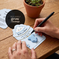 Baby in Bloom baby boy onesie seed paper with write, share, and grow message card - light blue design with pen writing personalized message, planting guide, and sprouting plant in background