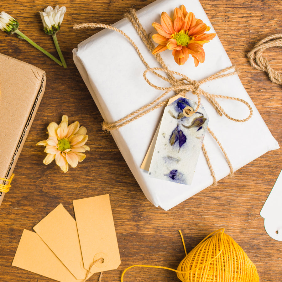 Purple Blank Tags Plantable Seed Paper by Seed Bloom Gifts tied to a white-wrapped gift with twine and accented by an orange mum flower.