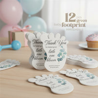 12 green Baby footprint seed paper baby shower favor by Seed Bloom Gifts with floral designs on a wooden surface with balloons and a gift in the background.