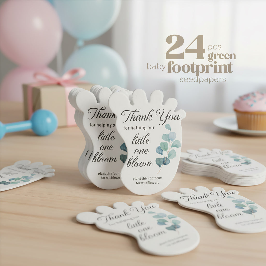 24 green Baby footprint seed paper baby shower favor by Seed Bloom Gifts with floral designs on a wooden surface with balloons and a gift in the background.