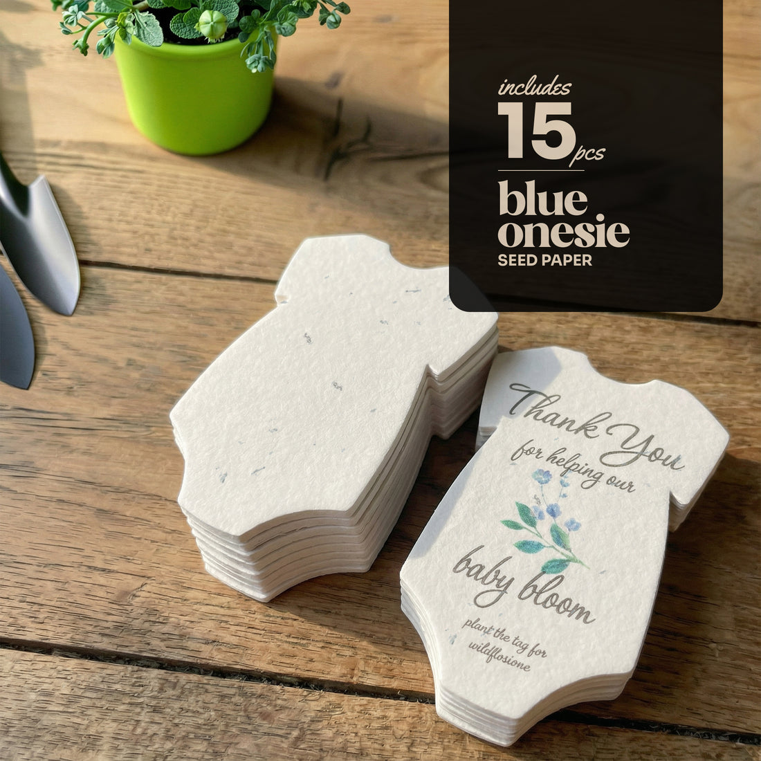 Stack of blue plantable seed paper onesie baby shower favors by Seed Bloom Gifts on a wooden table, with printed message “Thank you for helping our baby bloom” and text indicating the set includes 15 pieces.