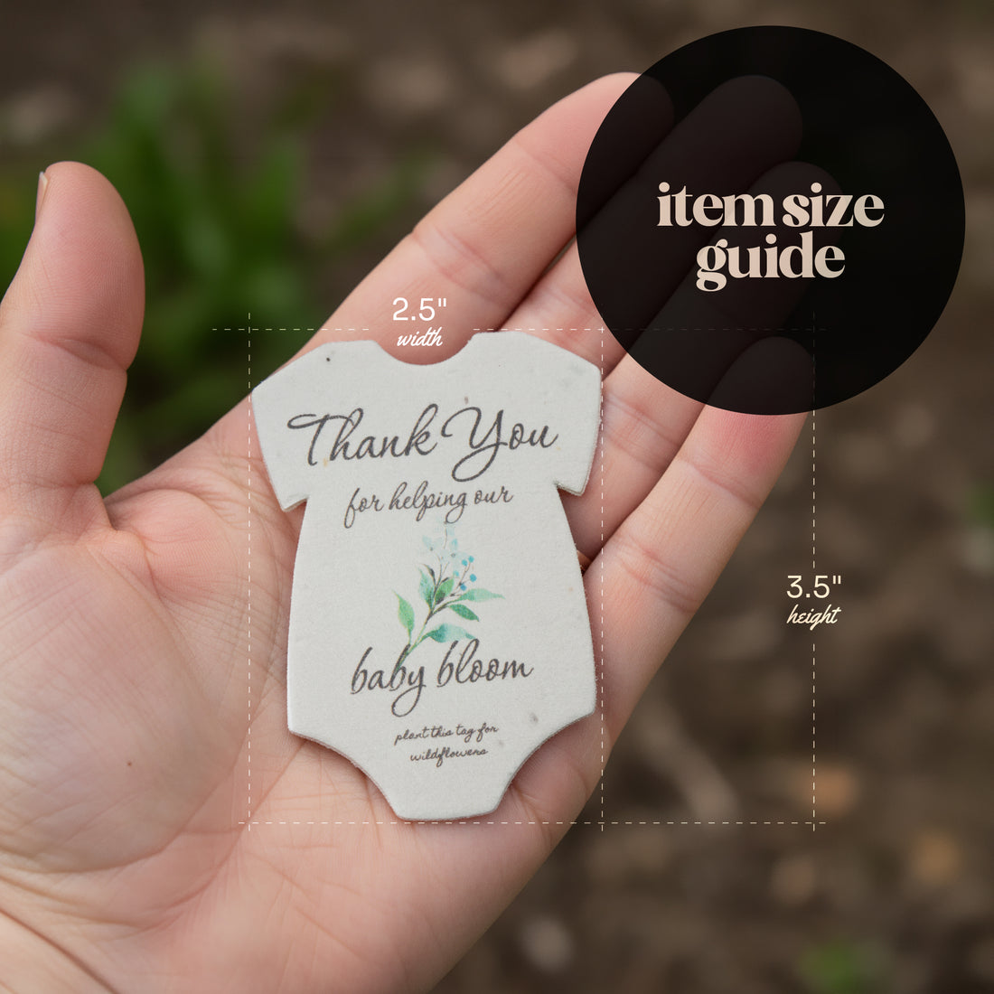 Hand holding a small, card-shaped baby onesie baby shower favor seed paper by Seed Bloom Gifts, featuring text and measurements.