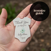 Hand holding a small, card-shaped baby onesie baby shower favor seed paper by Seed Bloom Gifts, featuring text and measurements.