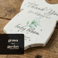 Seed paper baby onesie baby shower favor by Seed Bloom Gifts product with text and floral design on a wooden surface