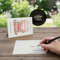 Mother's Day Bloom Card: Greeting card with flower shop illustration displayed on wooden table in garden setting, hand writing a message on card with fountain pen, featuring a quote bubble reading 'write a message that stays in the heart.