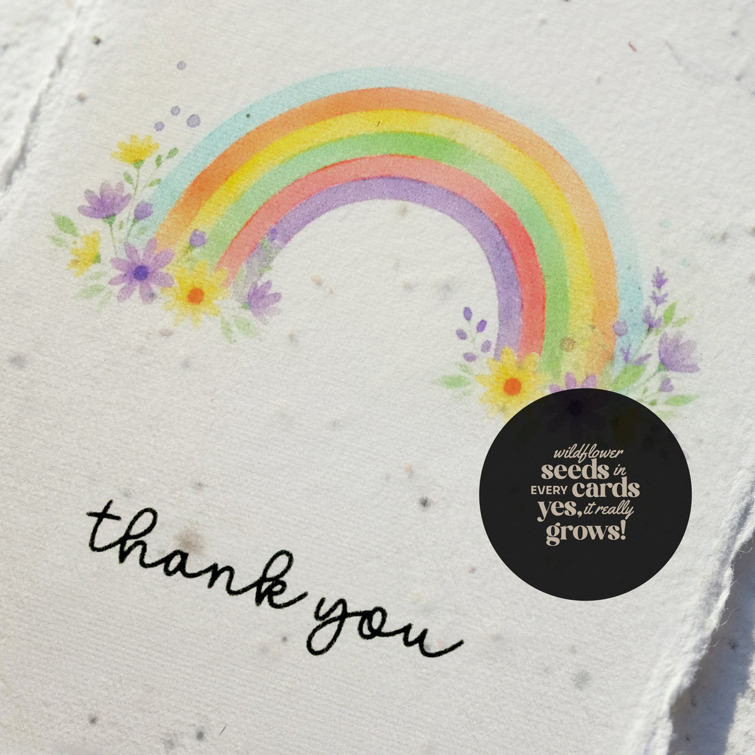 Seed paper thank you card featuring watercolor rainbow design with purple, yellow, and wildflower illustrations on cream seed paper, displaying &
