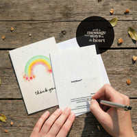 Seed paper thank you card opened showing front and back design with watercolor rainbow and wildflowers, featuring SeedBloom branding and planting instructions