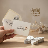 Hand holding a sympathy card with an envelope on a wooden surface, text 'A Thoughtful Tribute for Loved Ones' above by Seed Bloom Gifts
