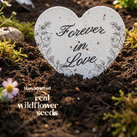Heart-shaped decorative stone with 'Forever in Love' text on a bed of soil with wildflowers by Seed Bloom Gifts