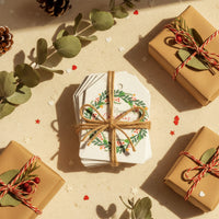 Rustic Christmas Holiday Gift  by Seed Bloom Gifts, wrapping flat lay. Eco-friendly tags with "Merry Christmas" wreath design, twine, and kraft paper.