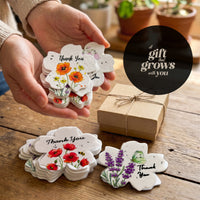 Seed paper thank you tags gift display showing scalloped flower-shaped cards with watercolor botanical designs held in hand and arranged with kraft paper gift box