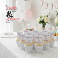 Baby shower setup with white and pink pots, featuring plantable seed paper baby shower favors by Seed Bloom Gifts, complete with 'onesie' and 'terracota' branding.