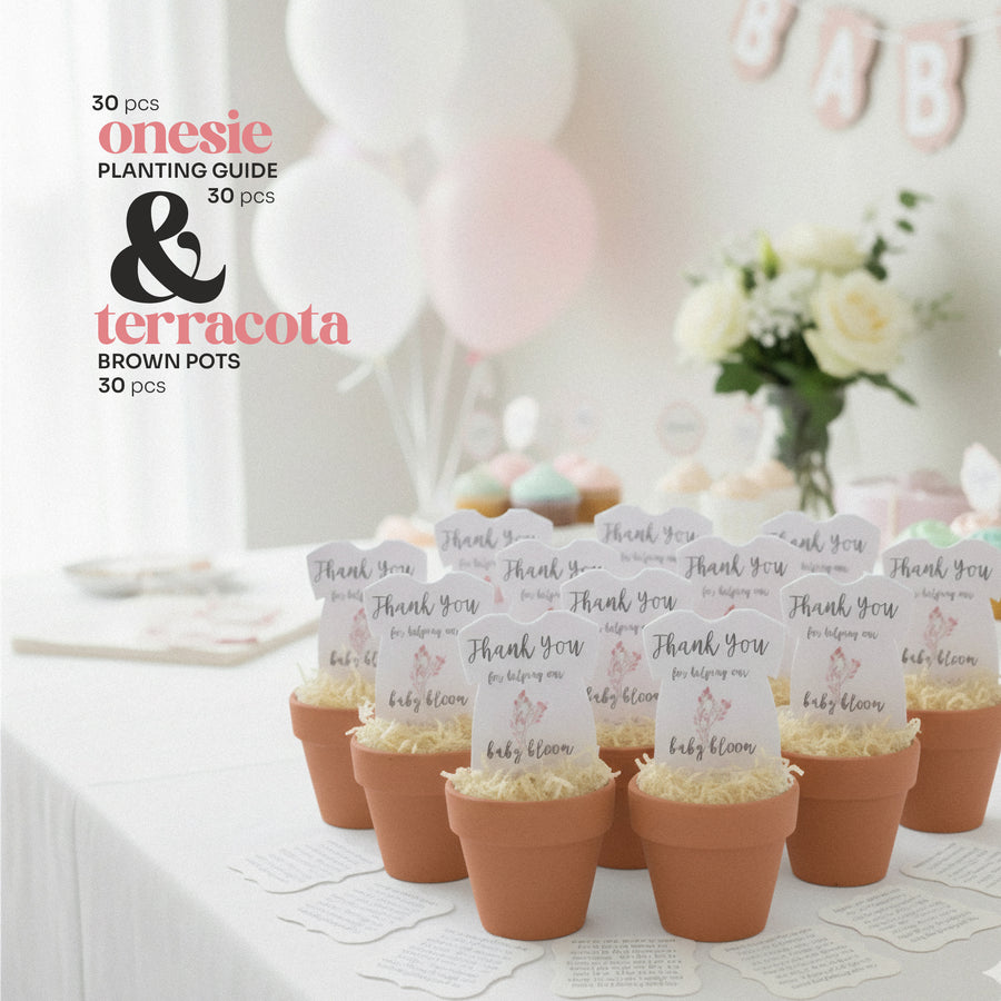 Terracotta pots with pink onesie plantable seed paper baby shower favor by Seed Bloom Gifts, planting guides, and baby shower decorations on a table.