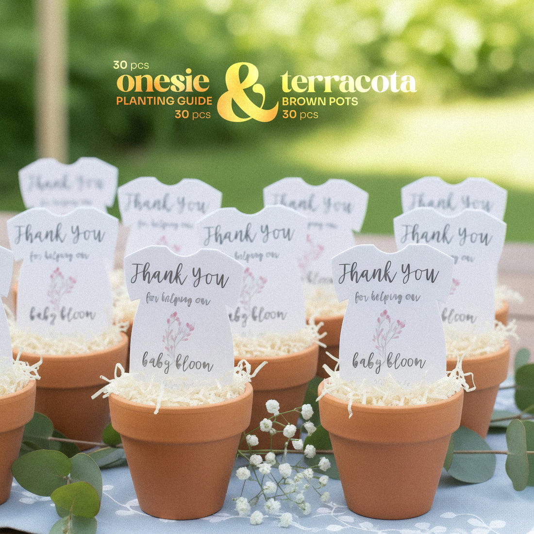 Terracotta pots with pink onesie plantable seed paper baby shower favors by Seed Bloom Gifts, and a blurred green outdoor background