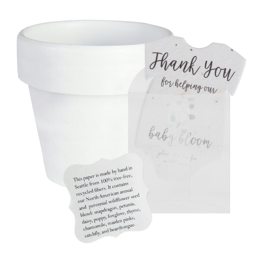 White pot next to a gender neutral green onesie plantable seed paper baby shower favor by Seed Bloom gifts, with a small card detailing the wildflower seed blend.