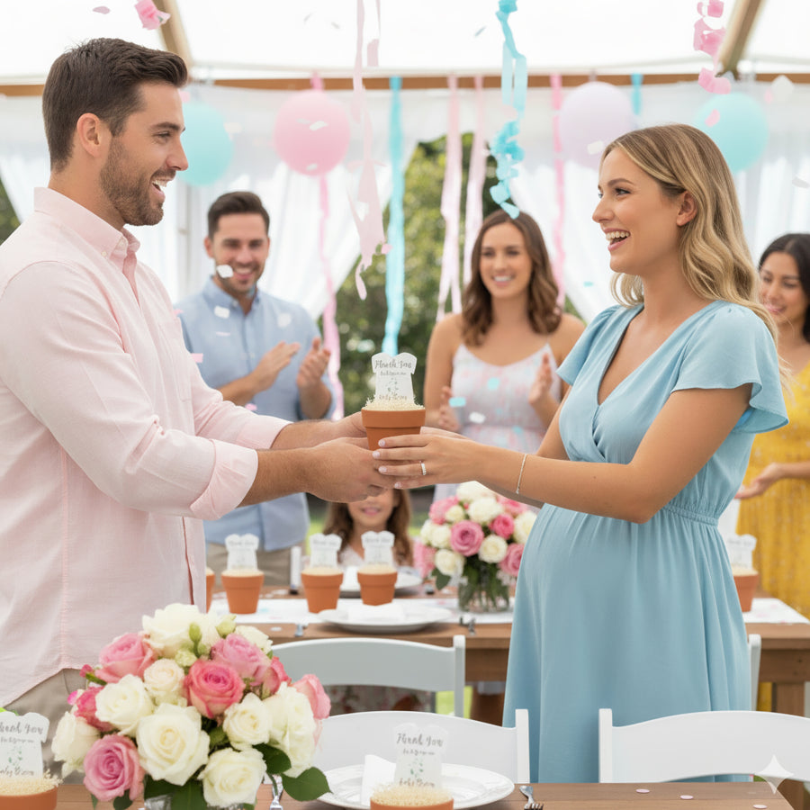 A pregnant woman in a blue dress accepts a terracotta potted favor from her husband at a baby shower decorated with pink and blue balloons and streamers. Guests smile and clap in the background. The table features the gender neutral green onesie plantable seed paper baby shower favor by Seed Bloom gifts as decorations and favors.