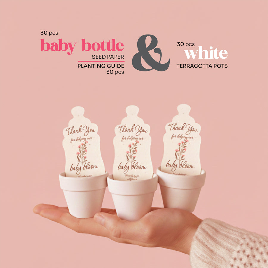 Three white baby bottle-shaped baby shower seed paper by Seed Bloom Gifts with 'Thank you for helping me bloom' text, held in a hand against a pink background.