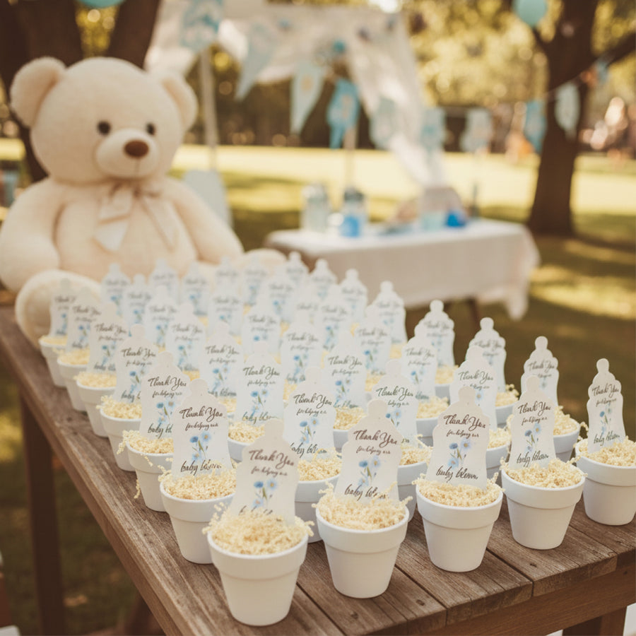 Table with baby shower decorations including teddy bear, bottles, and pots with baby bottle seed paper favor by Seed Bloom Gifts