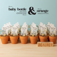 Set of terracotta pots with baby bottle seed paper by Seed Bloom Gifts  and wooden blocks on a light blue background