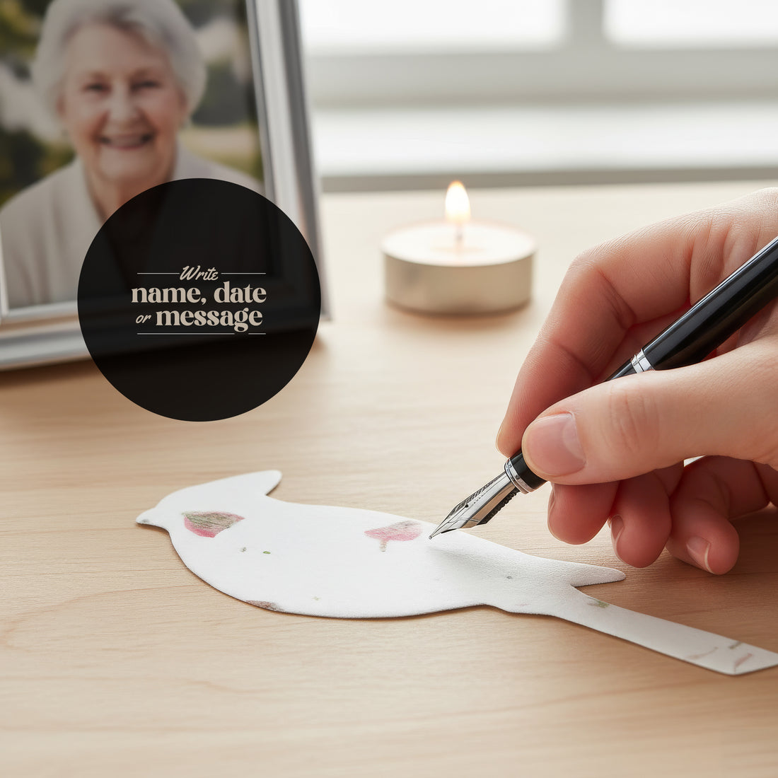 A hand writing on a white plantable seed paper dove funeral favor decorated with pressed pink flowers