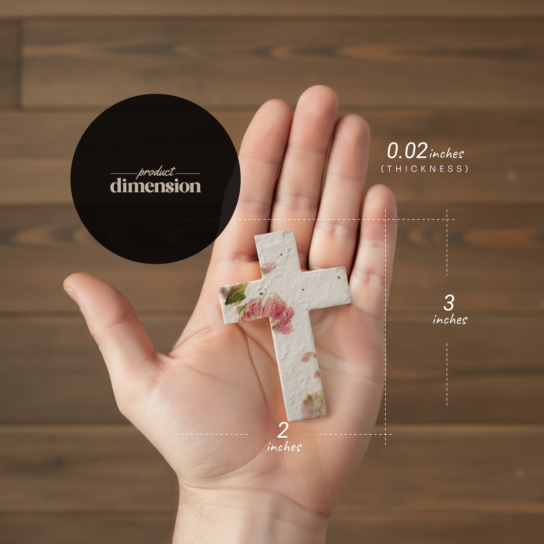 Hand holding a small cross with floral design, showing dimensions against a wooden background.