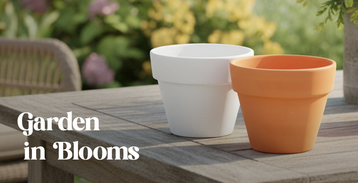 Two garden pots, one white and one orange, on a wooden table with blurred garden background.