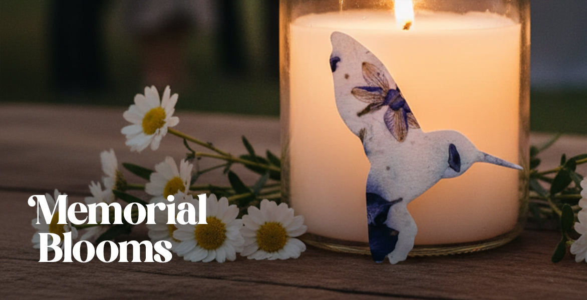 Candle with a butterfly decoration and flowers on a wooden surface, labeled 'Memorial Blooms'.
