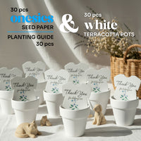 Set of 30 plantable seed paper onesie baby shower favors displayed in white terracotta pots with a planting guide, arranged on a neutral table setting with soft décor, each onesie reading “Thank you for helping our baby bloom