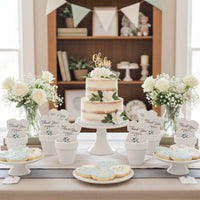 Elegant baby shower dessert table featuring a tiered “Oh Baby” cake, white floral arrangements, decorated cookies, and plantable seed paper onesie favors displayed in white pots across the table.