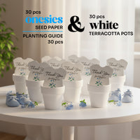 Set of 30 plantable seed paper onesie baby shower favors displayed in white terracotta pots on a round table, labeled as including seed paper onesies and a planting guide, each reading “Thank you for helping our baby bloom