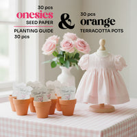 Set of seed paper onesies baby shower favors, terracotta pots, and a baby dress on a table with flowers in the background.